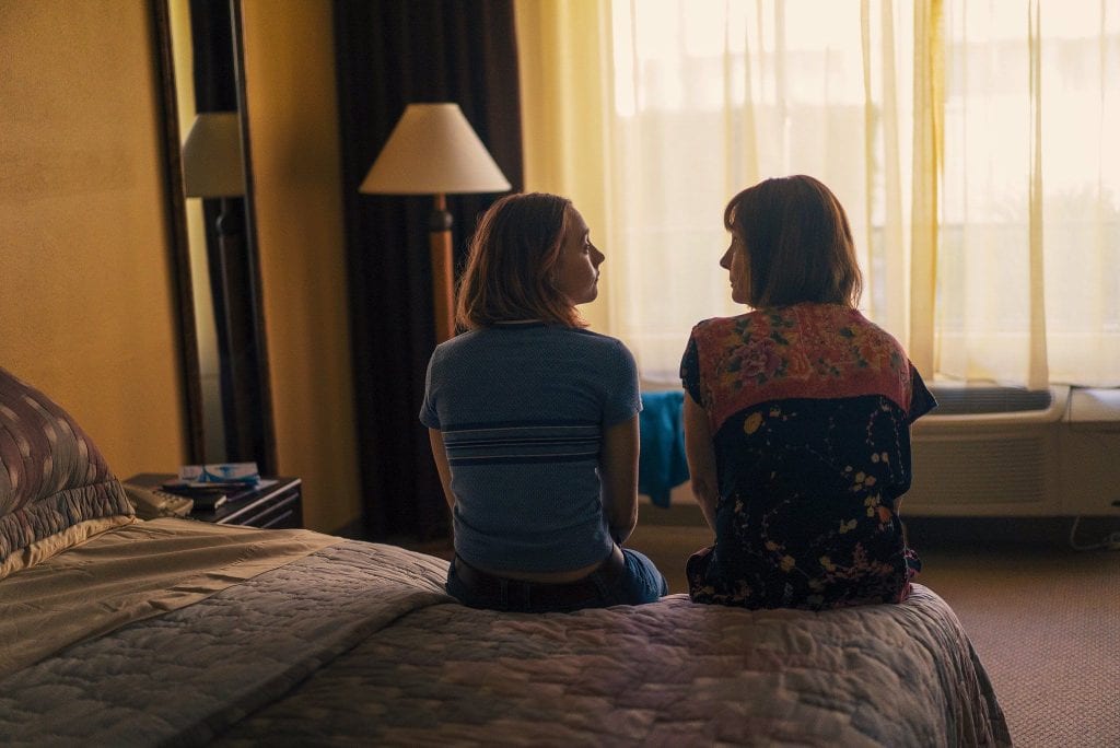 A teenager and her mother sitting on the side of a bed, looking at each other.
