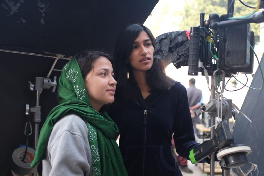 Ghazaal, the lead actress, and Ragini, the director, standing behind the scenes looking at some film equipment.
