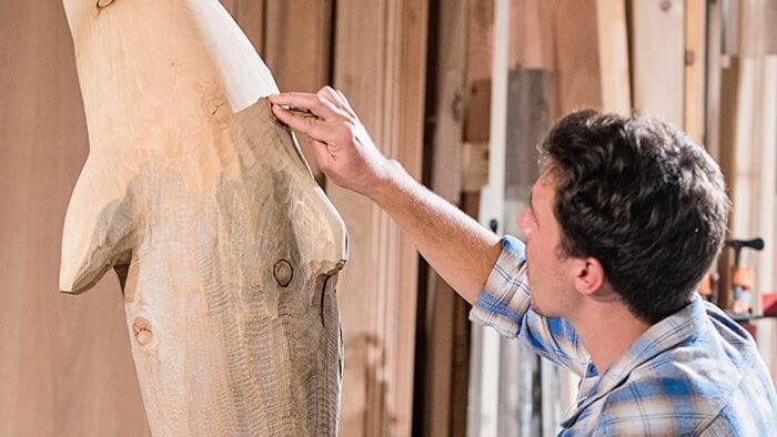 Mitch working on a wooden sculpture in an outdoor workshop.