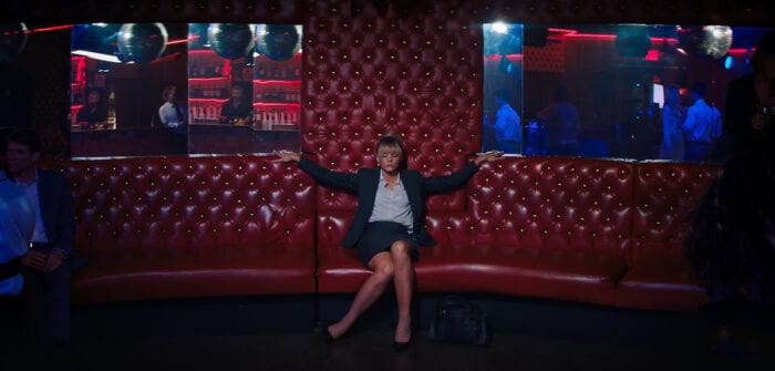 A still from Promising Young Woman where the main character sits alone in a dark club in work clothes. 