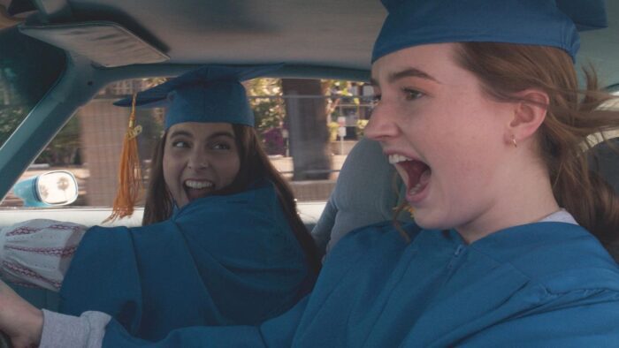 Amy and Molly scream as they drive to graduation, wearing matching blue caps and gowns.