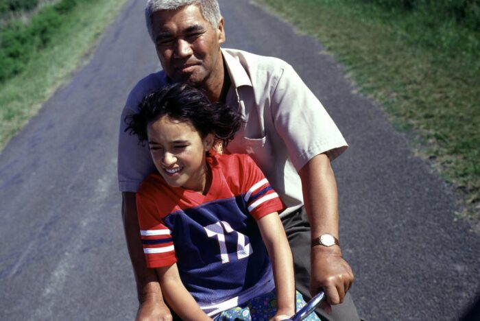 Pai sits in front of her grandfather on a bike, both of them squinting into the sun.