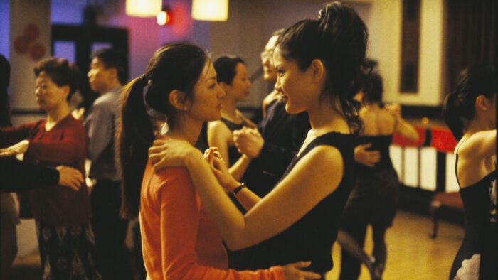 Vivian and Wil are holding and looking at each other in a room full of other people dancing. They look quite smitten and happy with each other. 