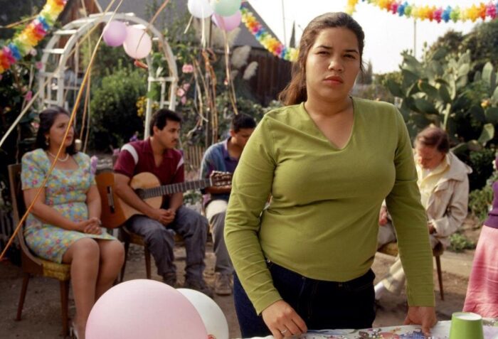 Ana stands, looking out at something while her graduation party happens behind her. 
